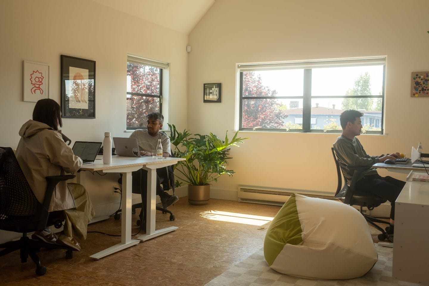 Três pessoas trabalhando em computadores, em um cômodo iluminado pelo Sol.